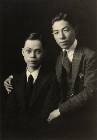 Black and white studio portrait of two well dressed Japanese American men—one man has his arm around the other.