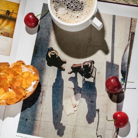 Photo of an aerial street scene reproduced in a book, with coffee, toast and marmalade, and cherries sitting on top. 